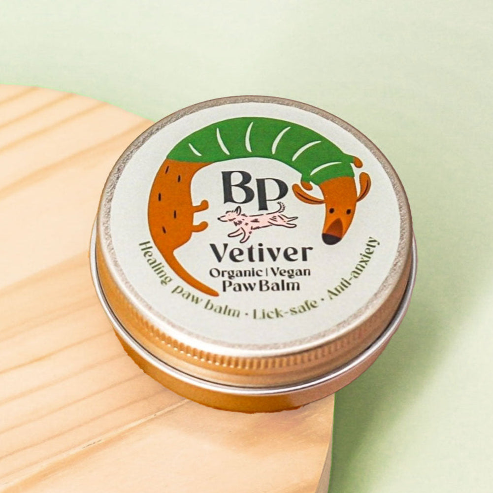 A round metal tin of BP Vetiver Organic Vegan Paw Balm resting on a light wood surface against a pale green background.